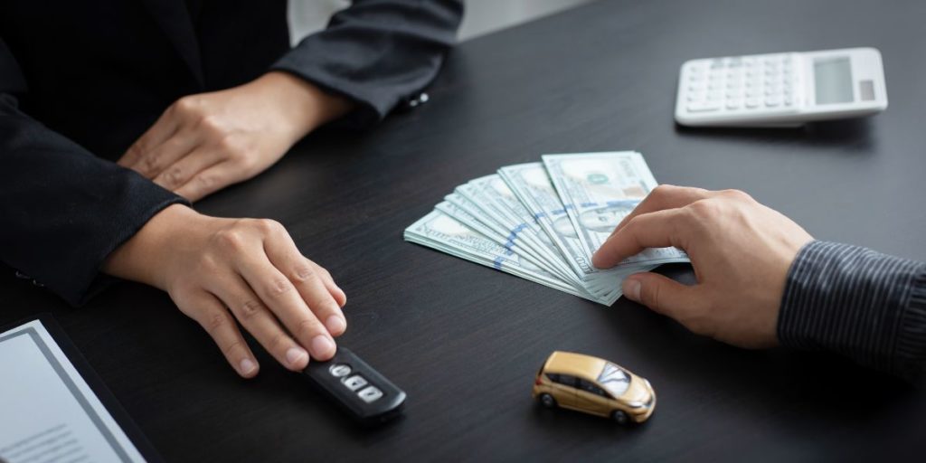 Hand holding cash with a mini car, representing how to sell your car for cash quickly with Ho Ho Buys Cars